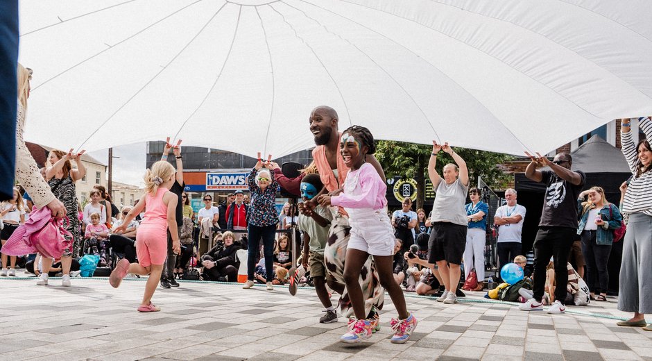 Two people running under a large parachute held by a group of people