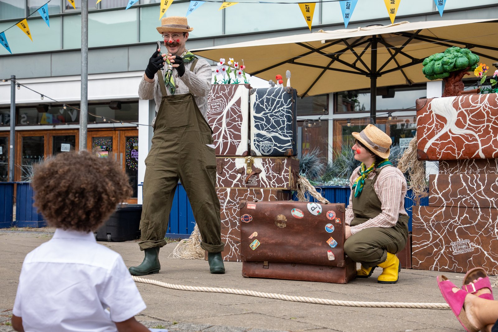 Man in green overall and hat next to woman kneeling down with suitcase