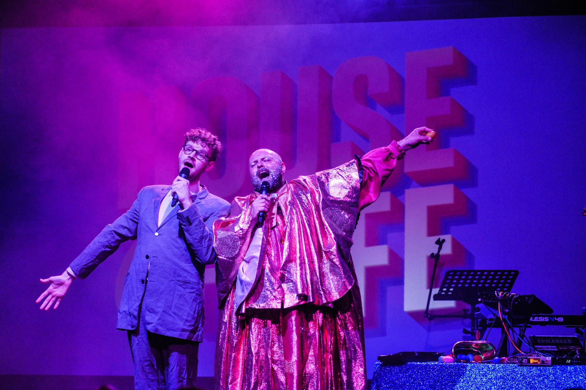 Two men on stage singing - one in a suit and one in shiny clothes